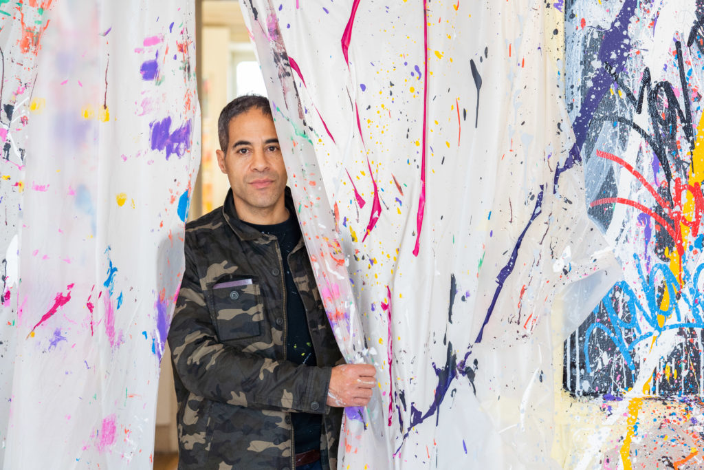 Portrait de l'artiste JonOne entre deux bâches avec des traces de peinture abstraite